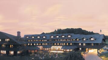 A large, multi-story hotel with a prominent central courtyard, surrounded by lush greenery and a mountainous backdrop.
