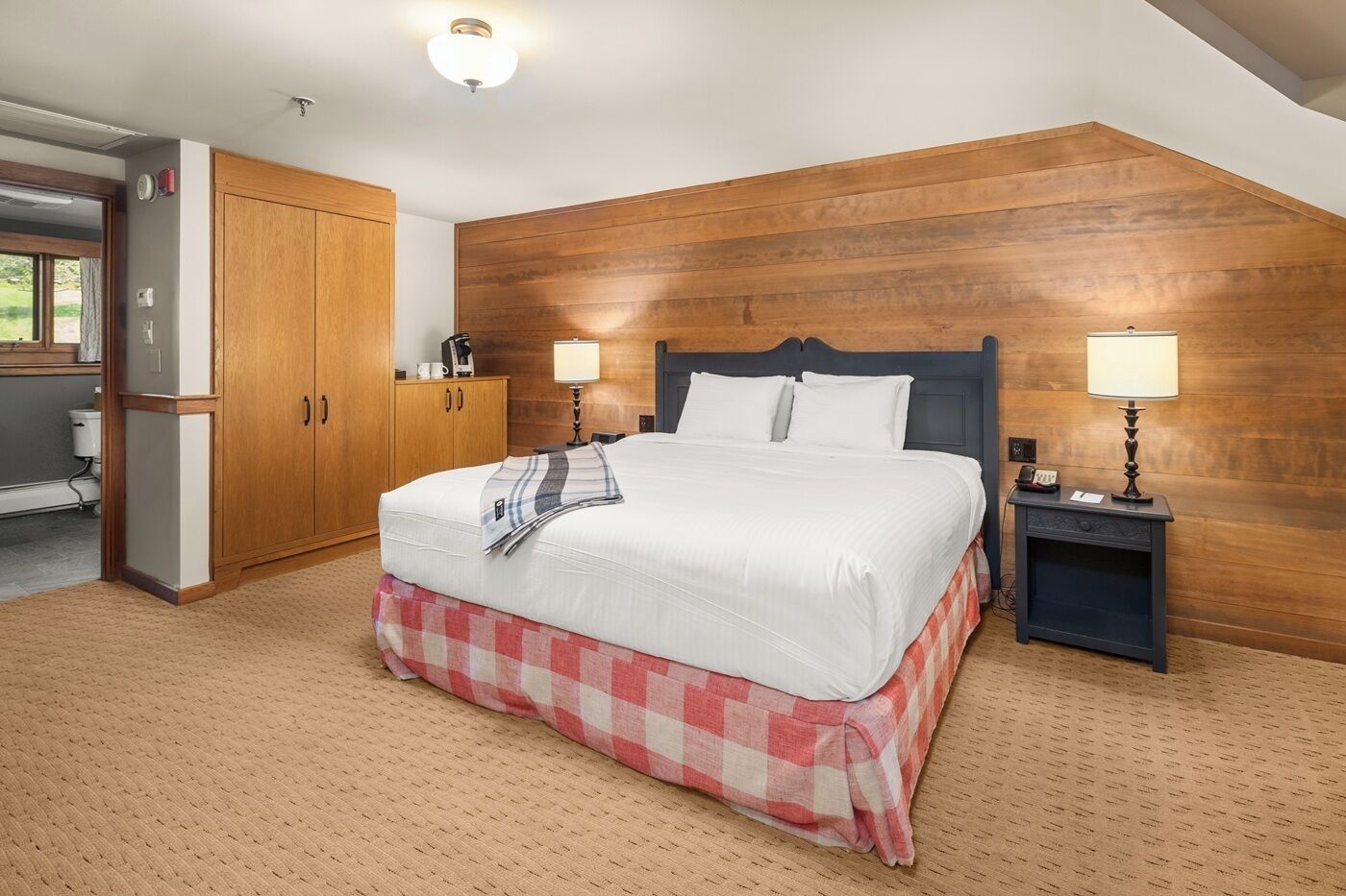 Une chambre à coucher comprenant un lit, une tête de lit en bois, deux tables de chevet avec des lampes, une armoire et un coin cuisine.