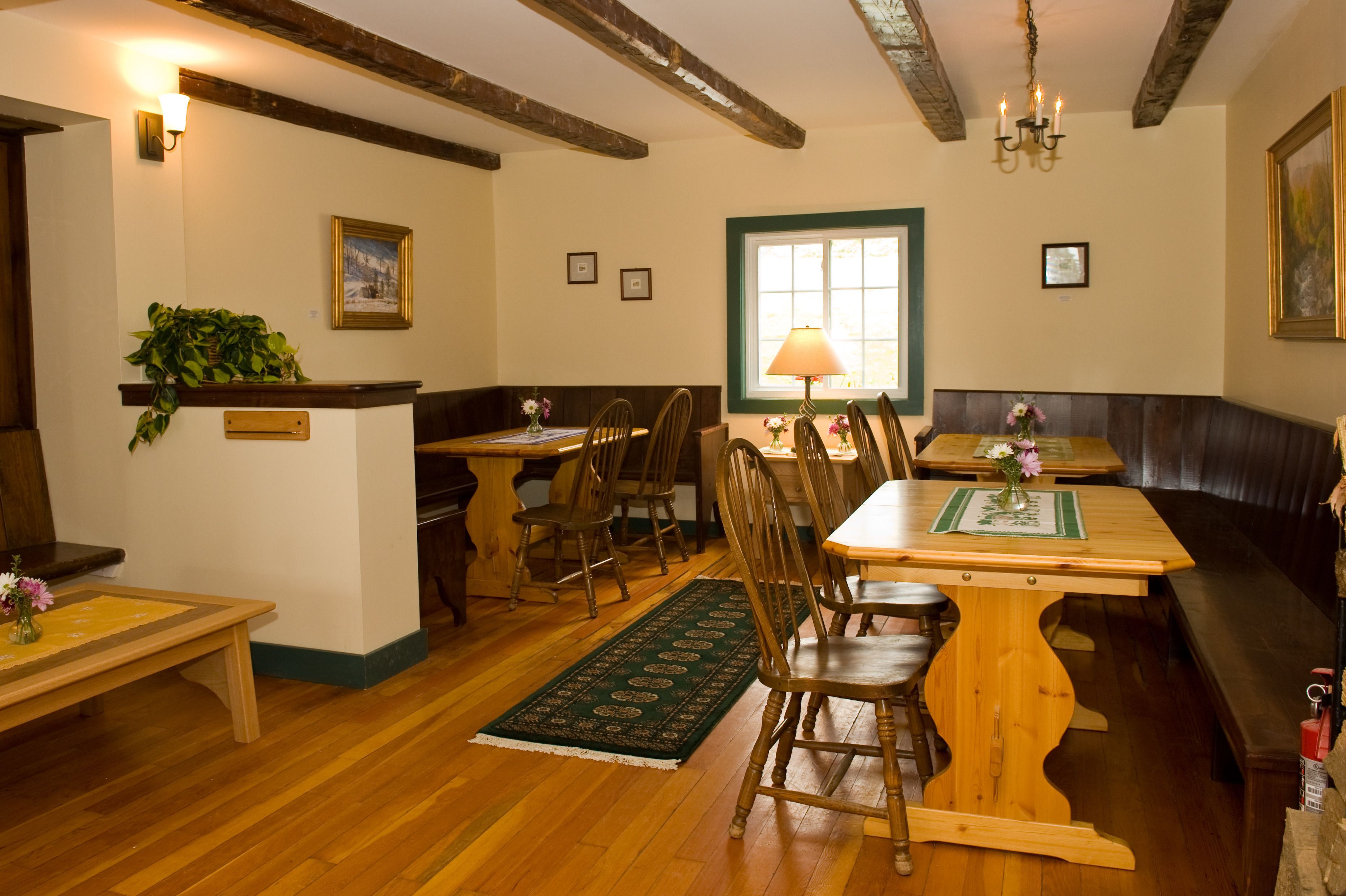 A dining area with wooden tables and chairs, a green rug, and a bench.