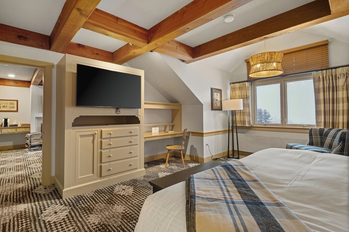 Une chambre à coucher comprenant un lit, un bureau avec une télévision, une chaise, une lampe sur pied et une fenêtre avec des rideaux.