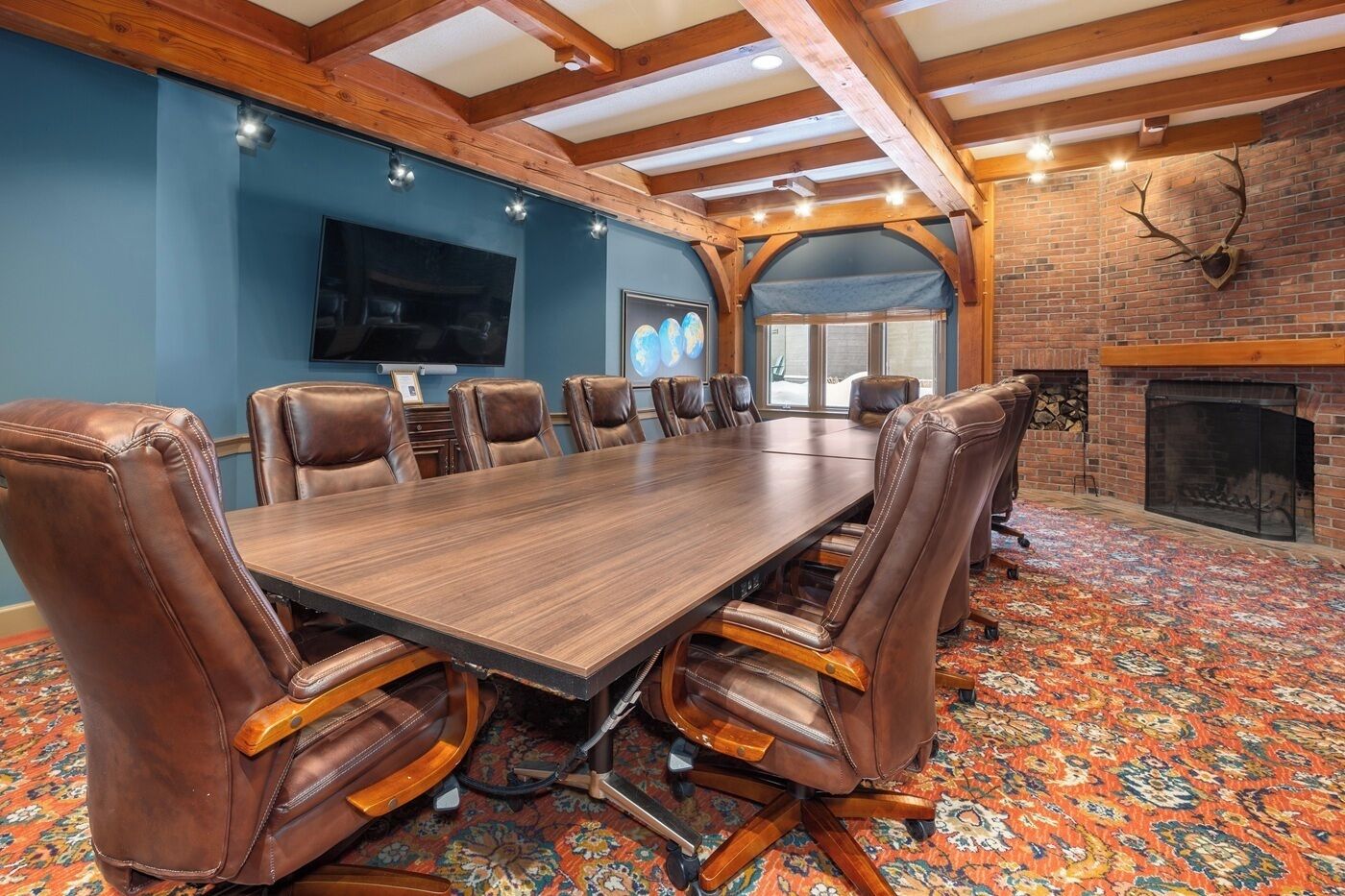 A conference room with a long table, leather chairs, a TV, and a fireplace.