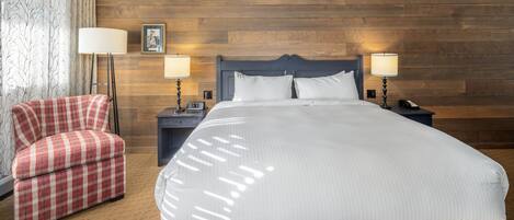 A hotel room with a large bed, two bedside tables, a red plaid armchair, and a wooden headboard.