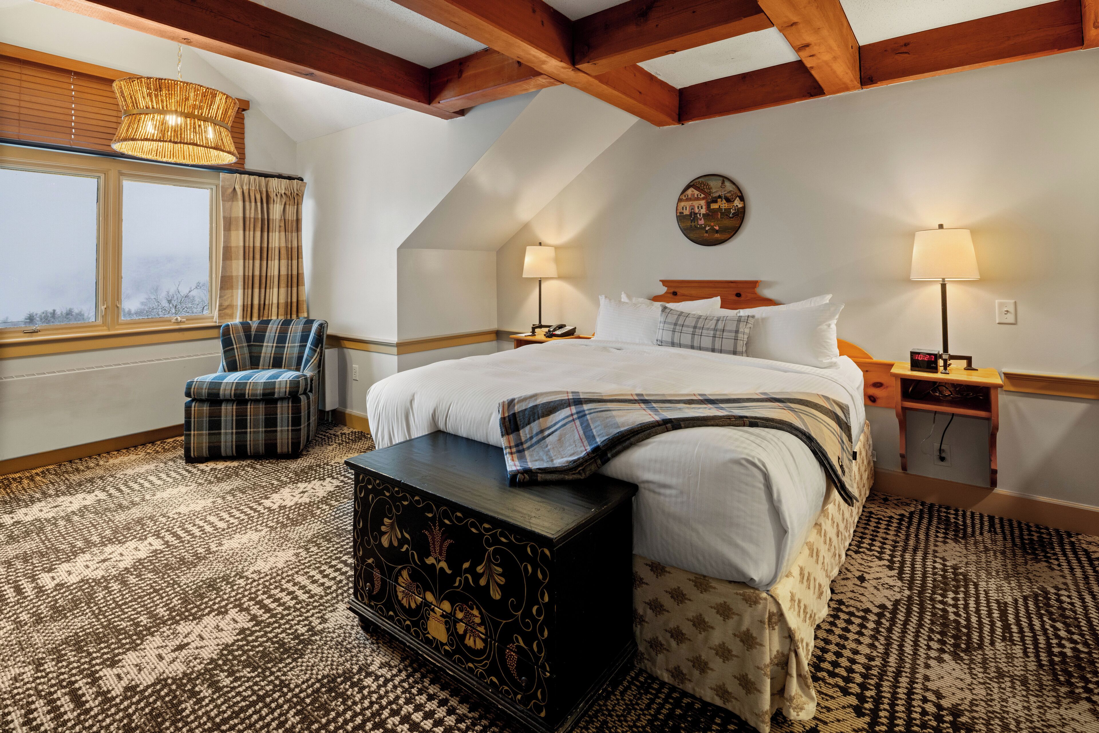 A bedroom with a large bed, a chest of drawers, a chair, a lamp, and a window with curtains.
