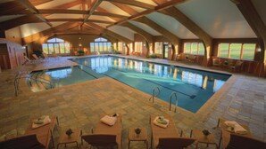 An indoor swimming pool with a high ceiling and wooden beams, surrounded by lounge chairs and tables. - von Trapp Family Lodge & Resort (Stowe)