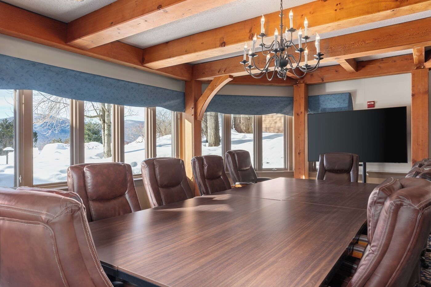A conference room with a large wooden table, leather chairs, and a chandelier.