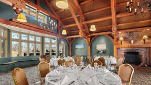 A dining room with round tables set for a meal, wooden beams on the ceiling, and a fireplace. - von Trapp Family Lodge & Resort (Stowe)