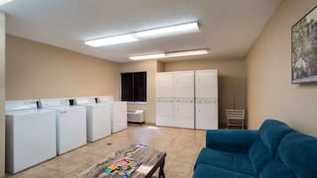 Un cuarto de lavado con varias lavadoras y secadoras, un sofá azul y piso de baldosas.
