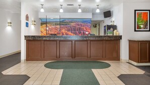 A reception area with a large painting of a forest landscape, a reception desk, and a green rug on the floor. - Americas Best Value Inn Cedar City (Cedar City)