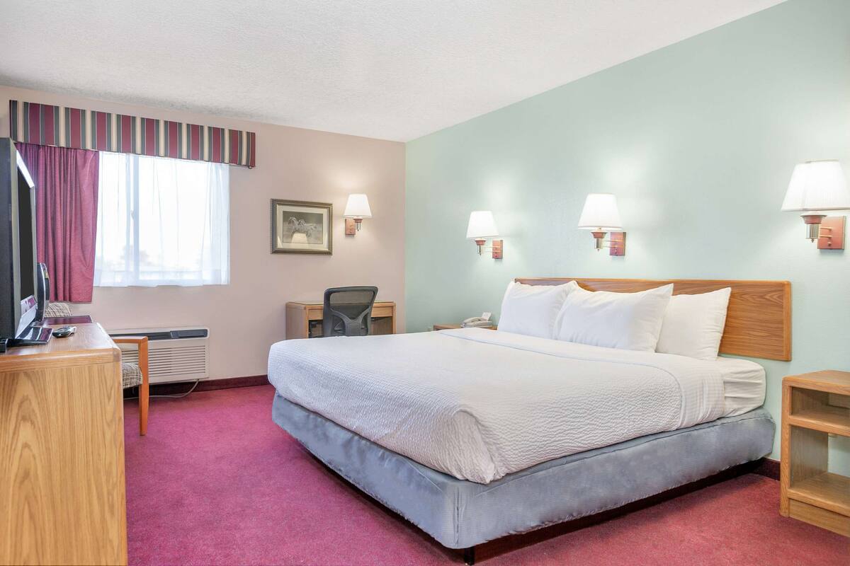 A hotel room with a large bed, a desk, a chair, and two bedside lamps.