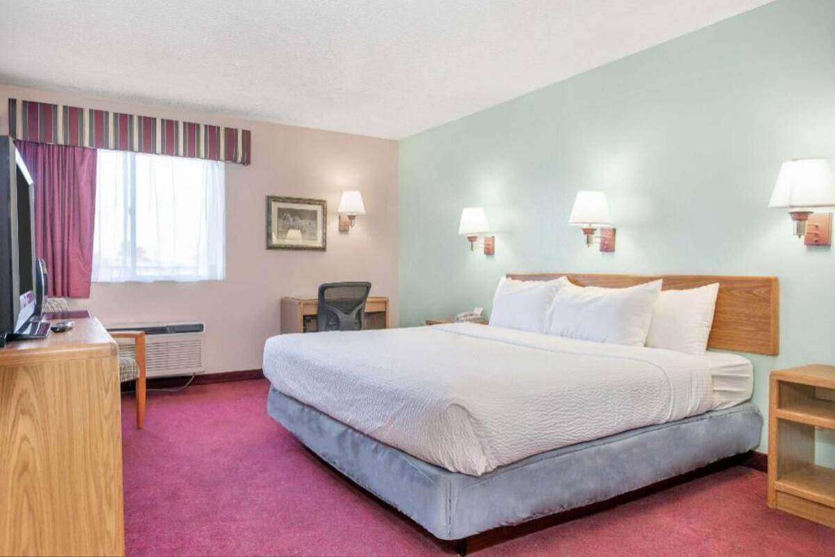 A hotel room with a bed, desk, chair, lamp, and a picture on the wall.