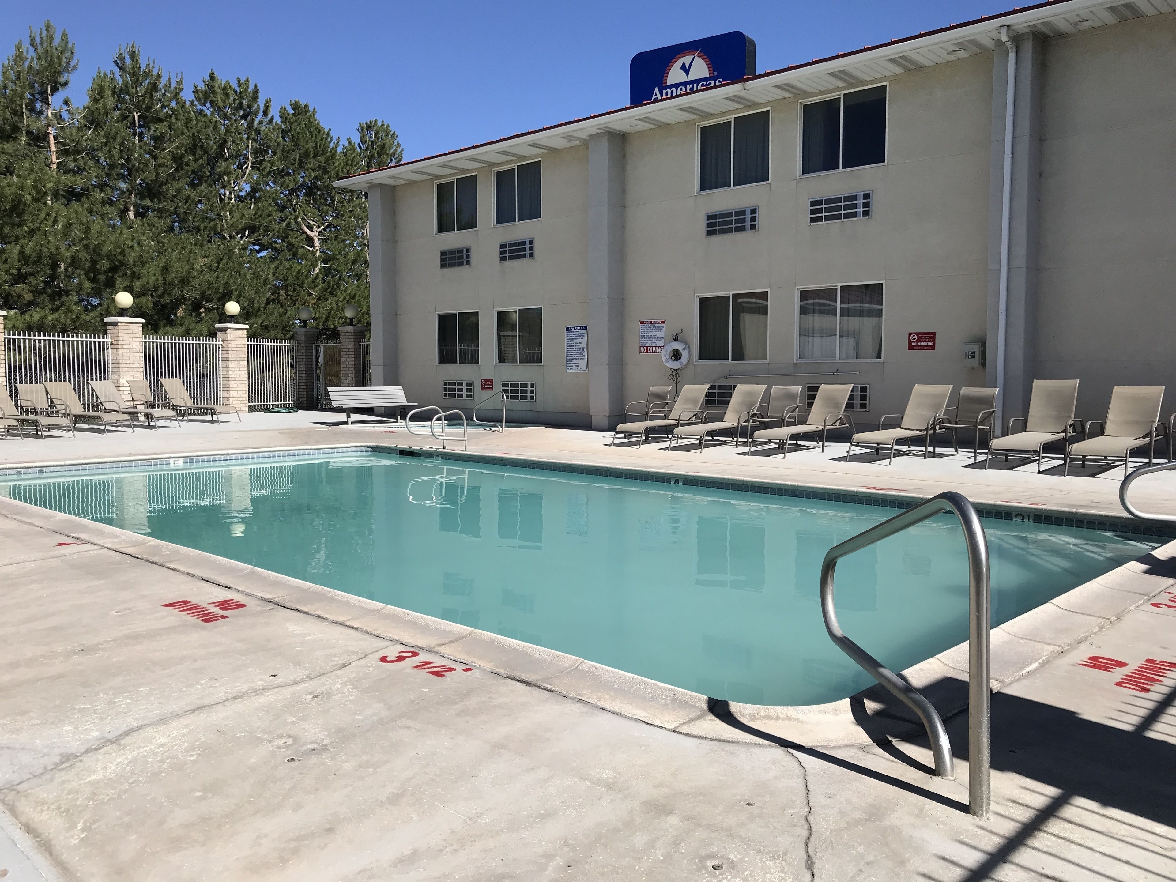 A swimming pool with lounge chairs and a lifeguard stand, surrounded by a building with a 'No Diving' sign.