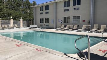 A swimming pool with lounge chairs and a lifeguard stand, surrounded by a building with a 'No Diving' sign.