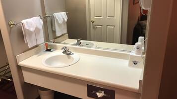 Une salle de bain d’hôtel avec un lavabo blanc, un miroir, un porte-serviettes avec deux serviettes, un flacon de savon liquide et une boîte de mouchoirs.