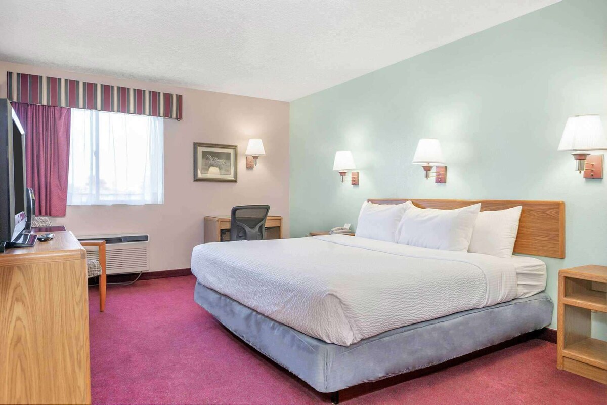 A hotel room with a bed, desk, chair, lamp, and a picture on the wall.