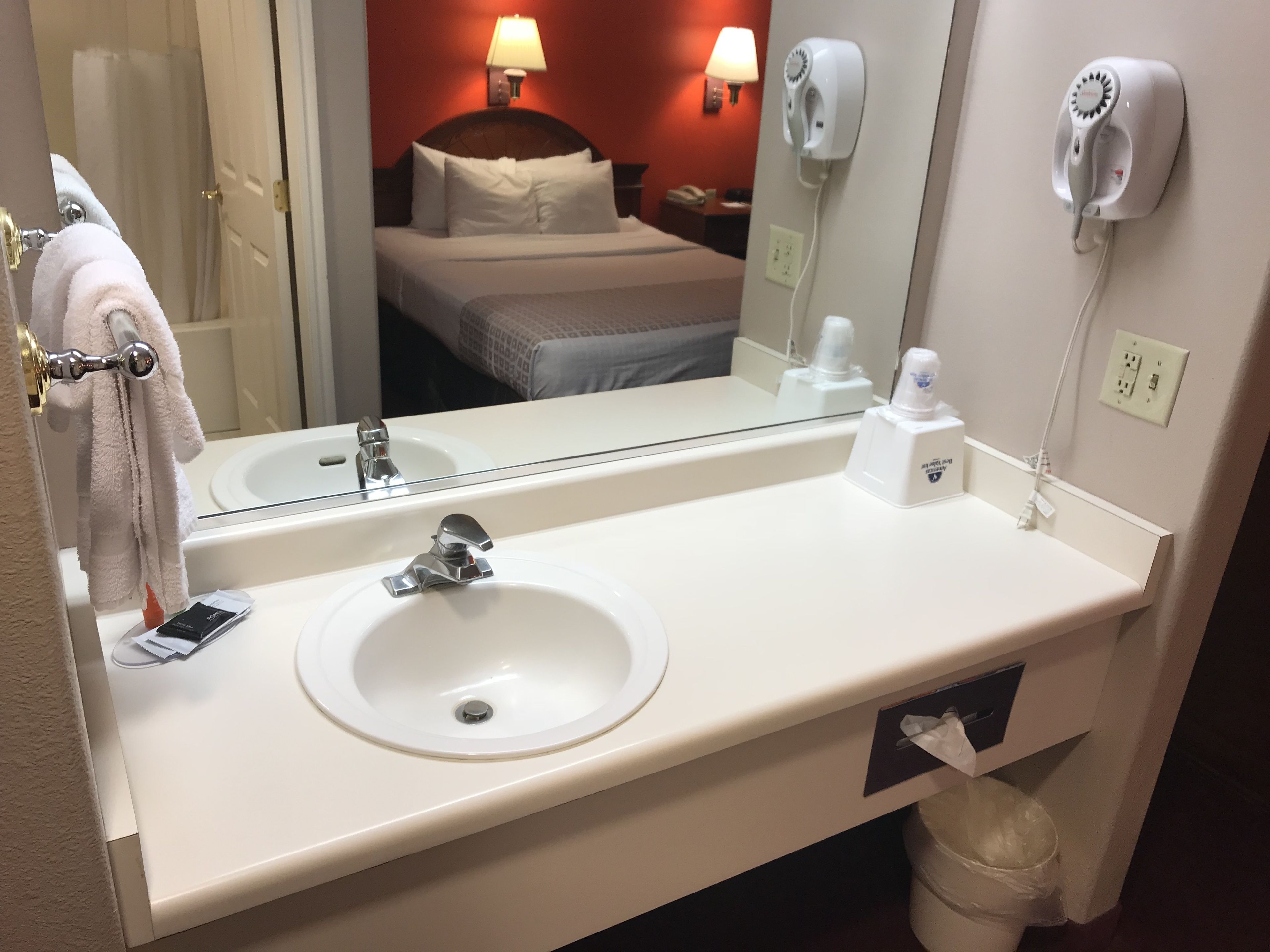 Un baño de hotel con un lavamanos blanco, un espejo, un secador de pelo y un perchero para toallas.