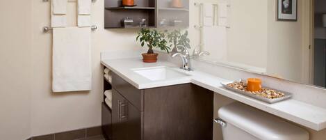 Un baño moderno con un lavabo blanco, armarios de madera oscura, una planta en maceta y un inodoro.