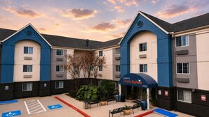 Ein Hotel mit blauer und beiger Fassade, einem überdachten Eingang und einem Parkplatz mit barrierefreiem Zugang.