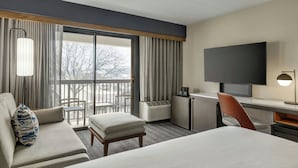 A hotel room with a bed, a desk, a TV, a chair, a sofa, a lamp, and a window with curtains. - Courtyard by Marriott Kokomo (Kokomo)