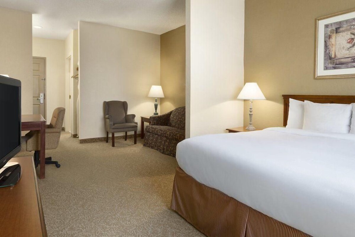 A hotel room with a large bed, a desk with a computer, two chairs, and two bedside lamps.