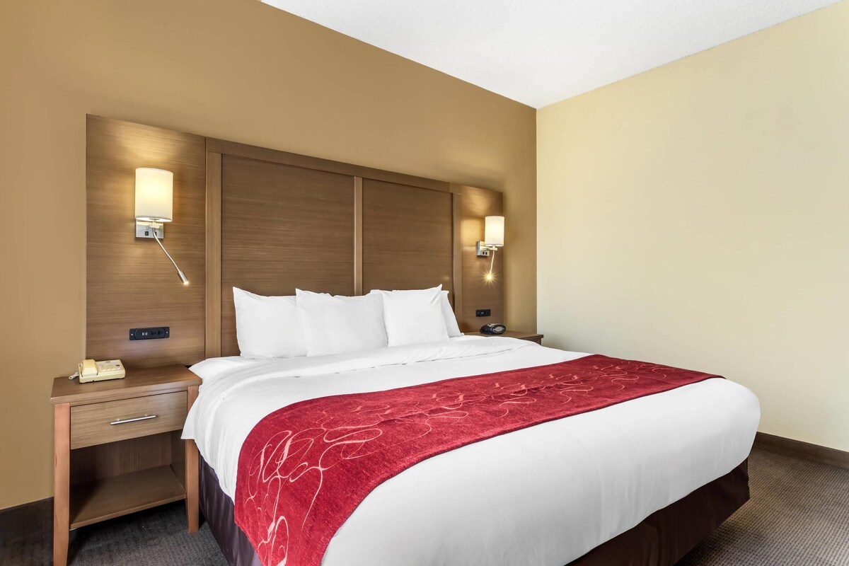 A hotel room with a large bed, two bedside tables, a red throw blanket, and wall-mounted lamps.