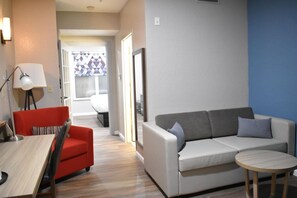A modern living room with a red sofa, a grey couch, a round wooden table, and a lamp. - Blue Hotel IAH (Houston)