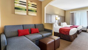 A hotel room with a grey sofa, two red pillows, a brown ottoman, a bed with a red bedspread, and a large window with curtains. - Comfort Suites Bush Intercontinental Airport (Houston)