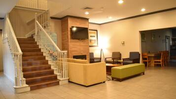 A hotel lobby with a staircase, seating area, and a television mounted on the wall.