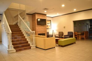 A hotel lobby with a staircase, seating area, and a television mounted on the wall. - Blue Hotel IAH (Houston)