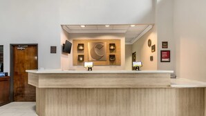 A reception desk with a wooden finish, two monitors, and a large wall clock. - Comfort Suites Bush Intercontinental Airport (Houston)