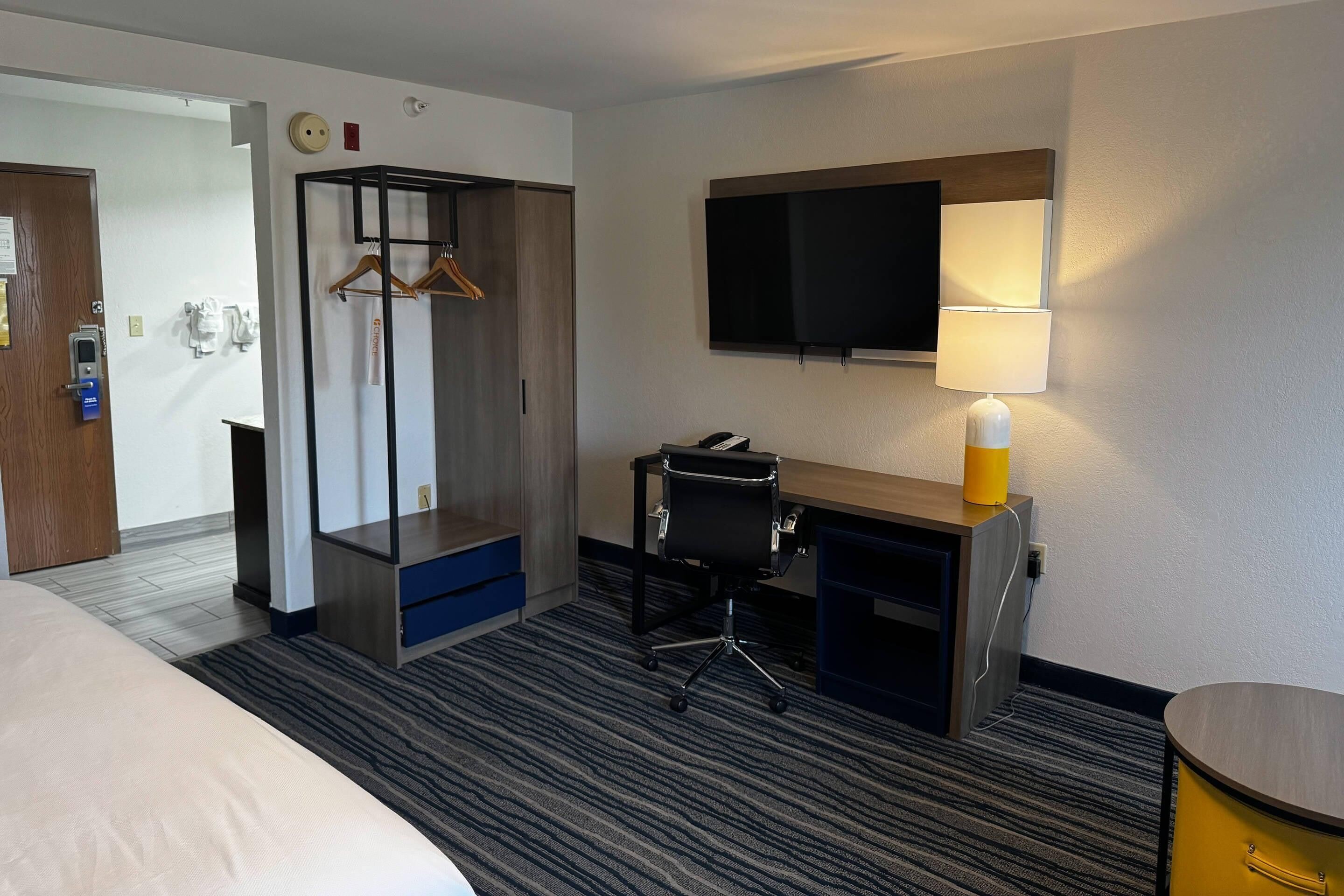 A hotel room with a bed, a desk with a chair, a television, and a lamp.