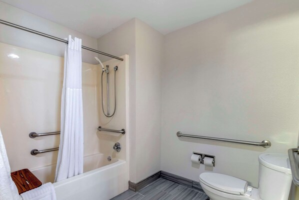 Un baño con bañera, ducha, inodoro y barras de apoyo.