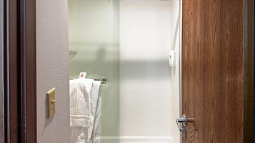 A shower with a glass door, a towel rack with a towel, and a wooden door.