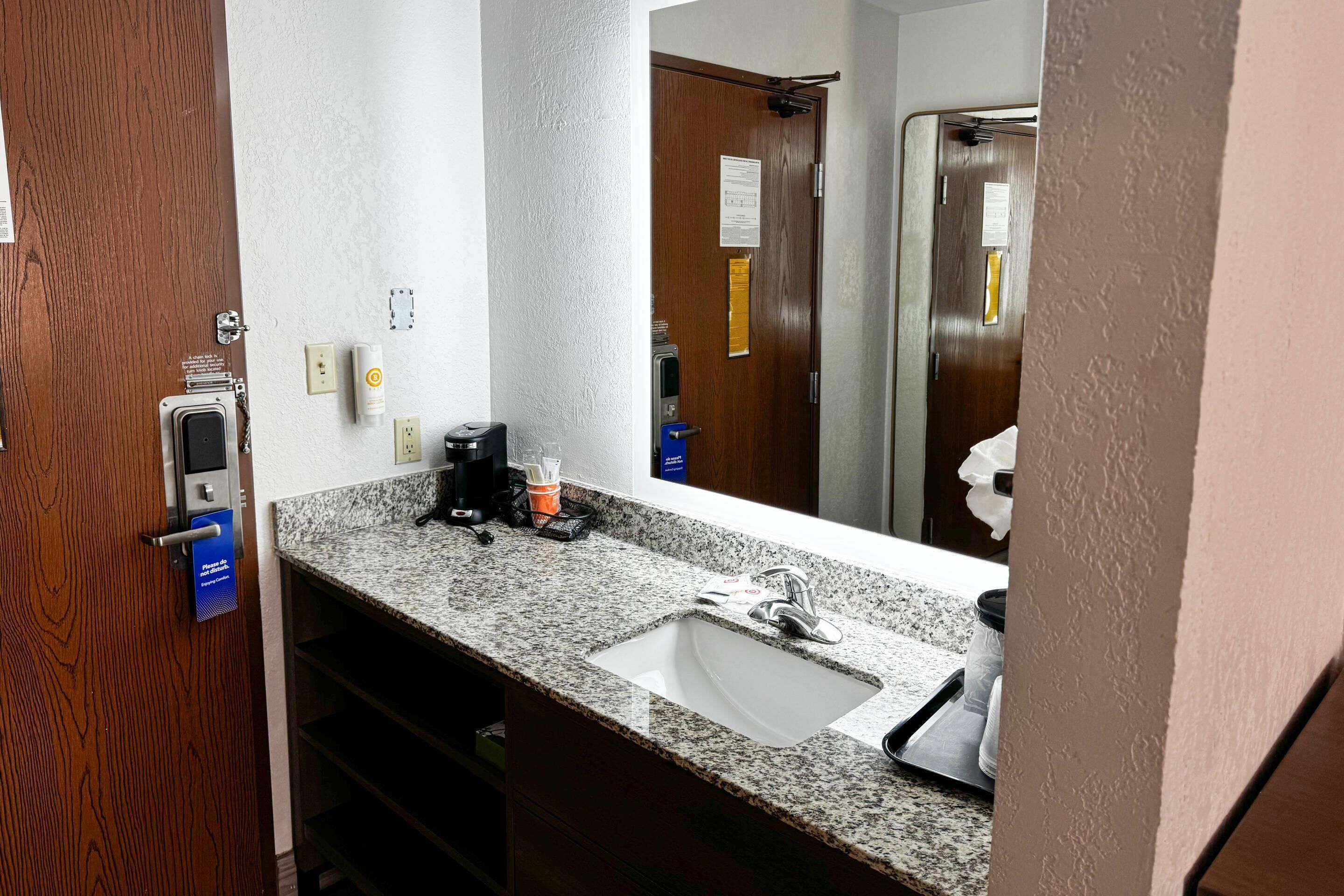 A bathroom with a granite countertop, a sink, a mirror, and a door with a towel rack.