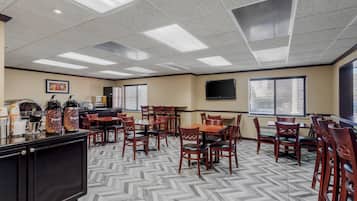 Un espace repas comprenant plusieurs tables et chaises, un coin café et un téléviseur fixé au mur.