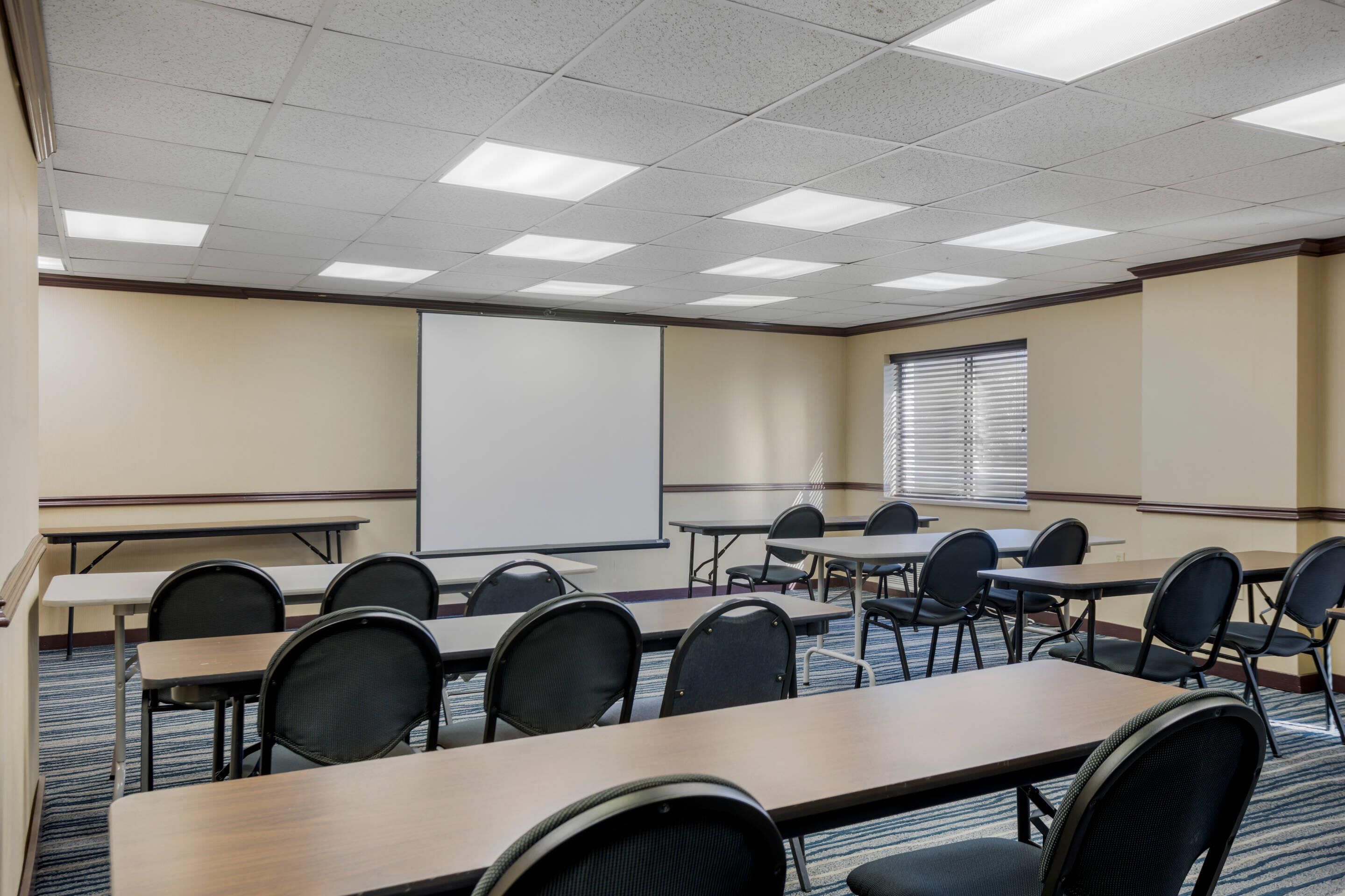 Un salón de conferencias con una pantalla de proyección grande, varias mesas y sillas.
