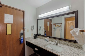 A hotel bathroom with a wooden door, a large mirror, a granite countertop, a sink, a towel rack, and a paper on the door.