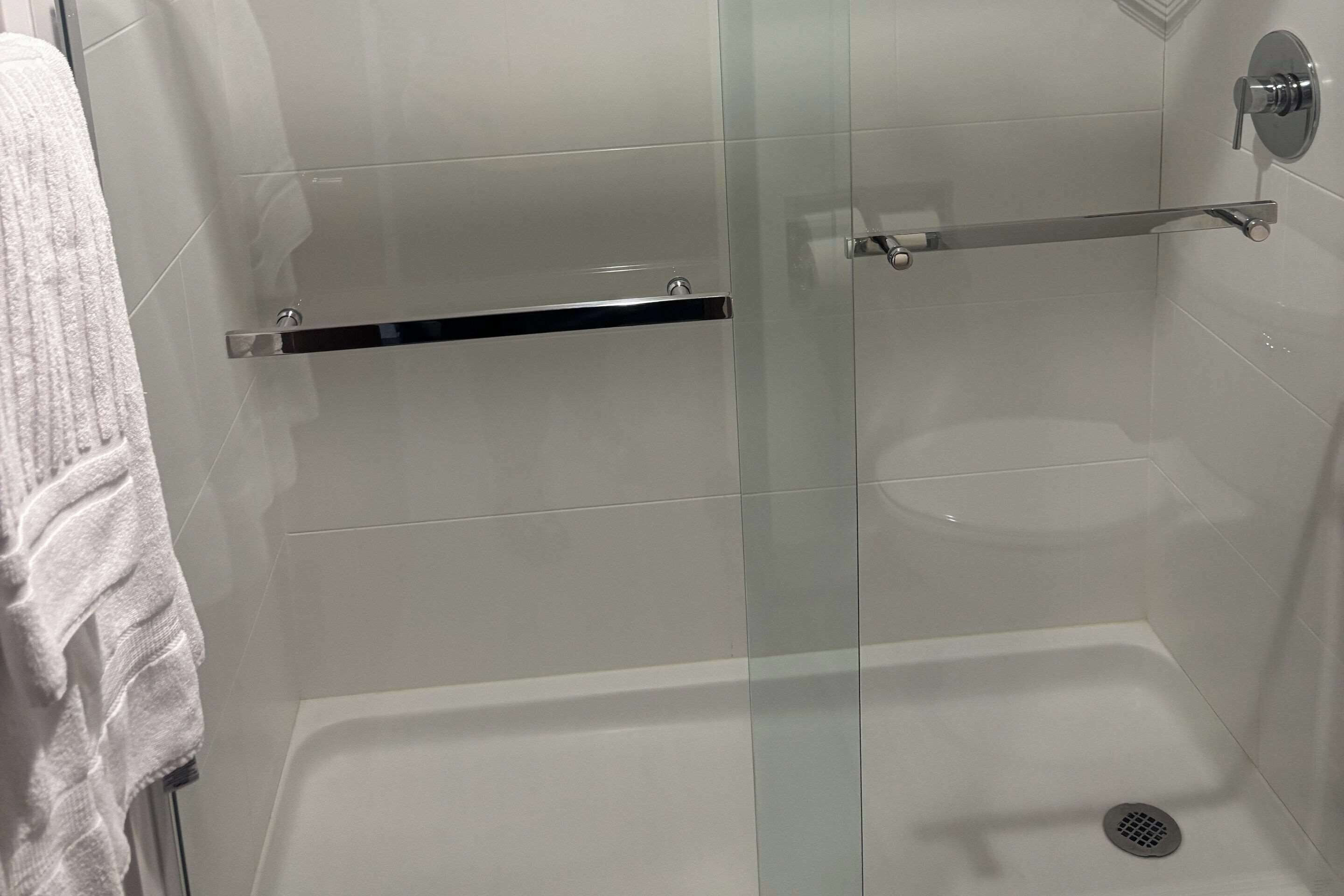A modern bathroom with a glass shower enclosure, a white bathtub, and a towel rack.