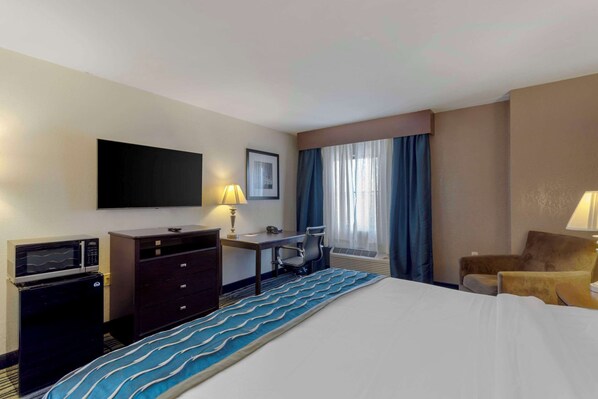 A hotel room with a bed, a desk, a chair, a television, and a microwave.