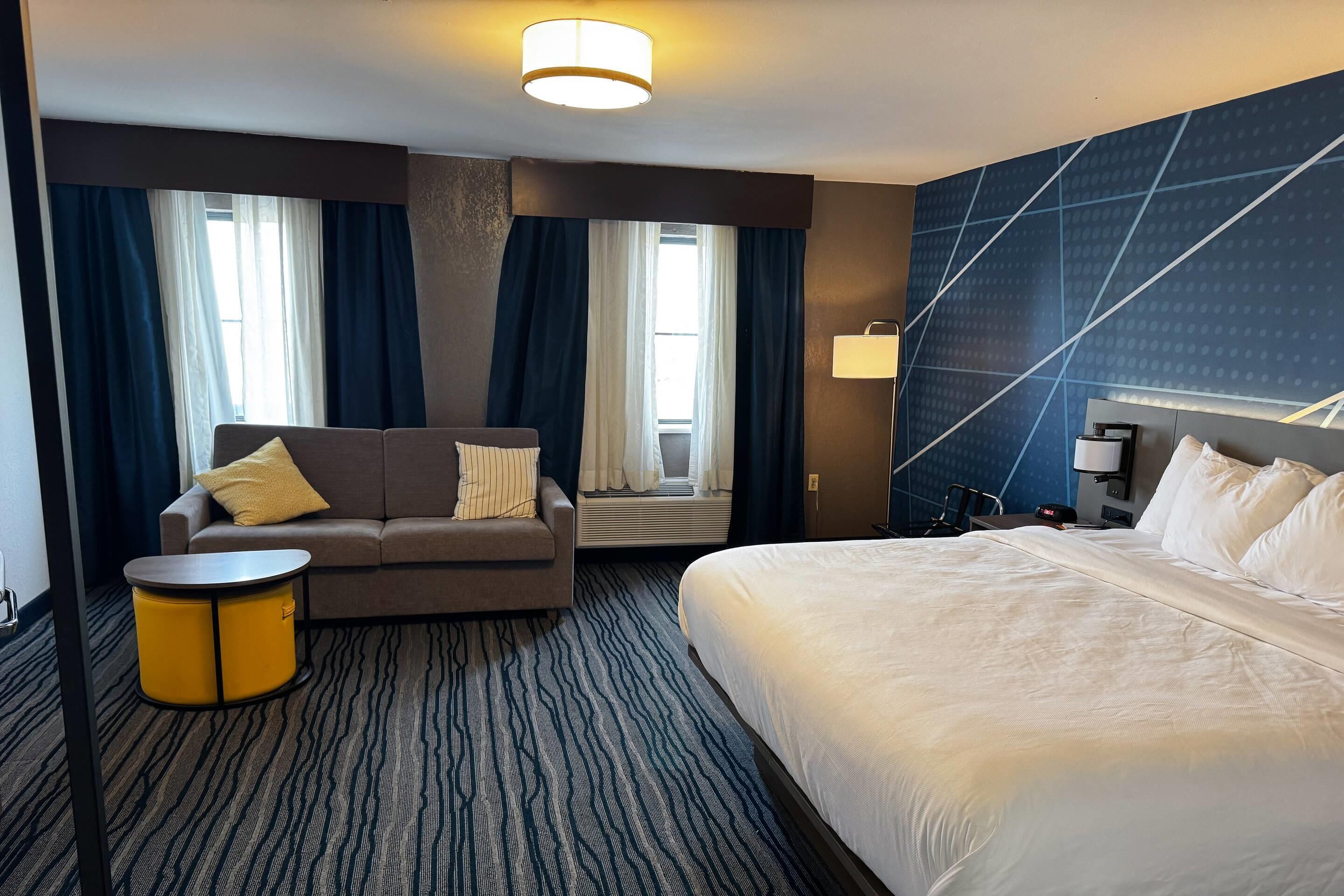 Una habitación de hotel con cama, sofá, una mesita y una lámpara de pared.