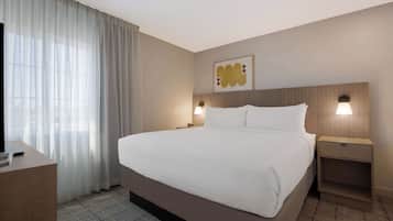 Habitación de hotel con una cama grande, un escritorio, un televisor y una ventana con cortinas translúcidas.