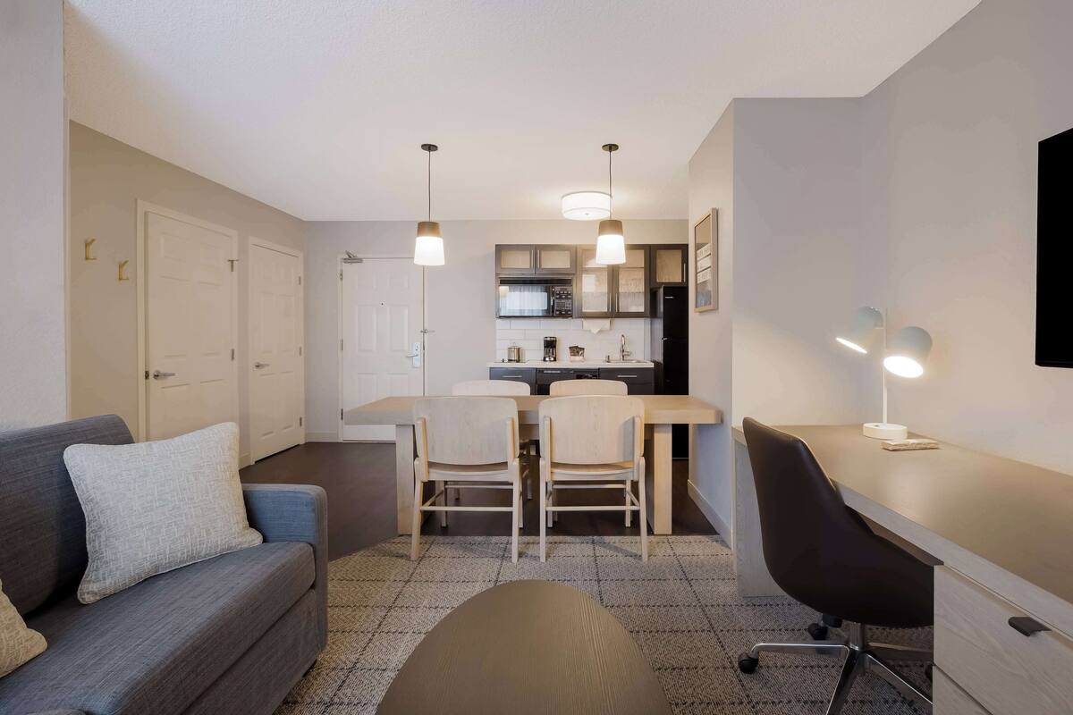 Un espace de vie compact comprenant un canapé, une table à manger, des chaises, un bureau et un coin cuisine.