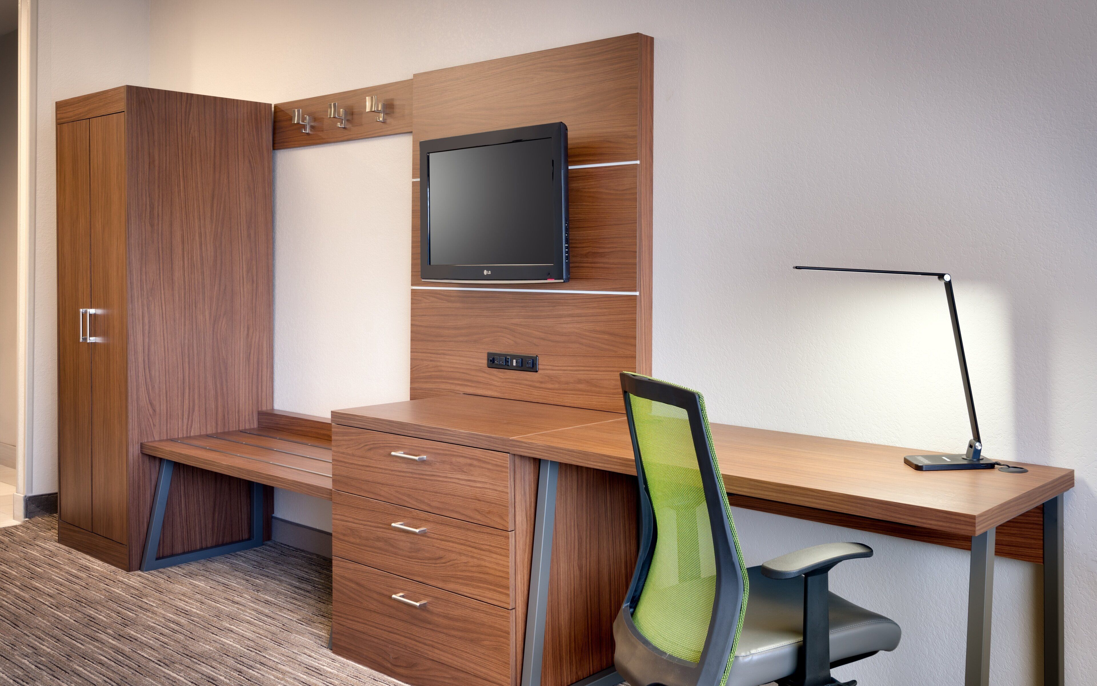 A modern office desk with a chair, a television mounted on the wall, and a desk lamp.