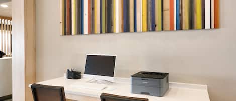 A workspace with a desk, two chairs, a computer, a printer, and a colorful abstract painting on the wall.