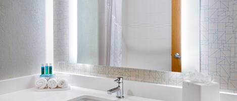A bathroom with a white sink, a mirror, a shower curtain, and toiletries on the counter.