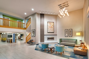 A spacious lobby with a high ceiling, a staircase, a fireplace, and a seating area with a sofa and chairs.
