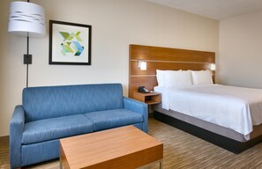 A hotel room with a bed, a blue sofa, a wooden coffee table, a nightstand with a phone, and a framed abstract art piece on the wall. - Holiday Inn Express Heber City by IHG (Heber City)