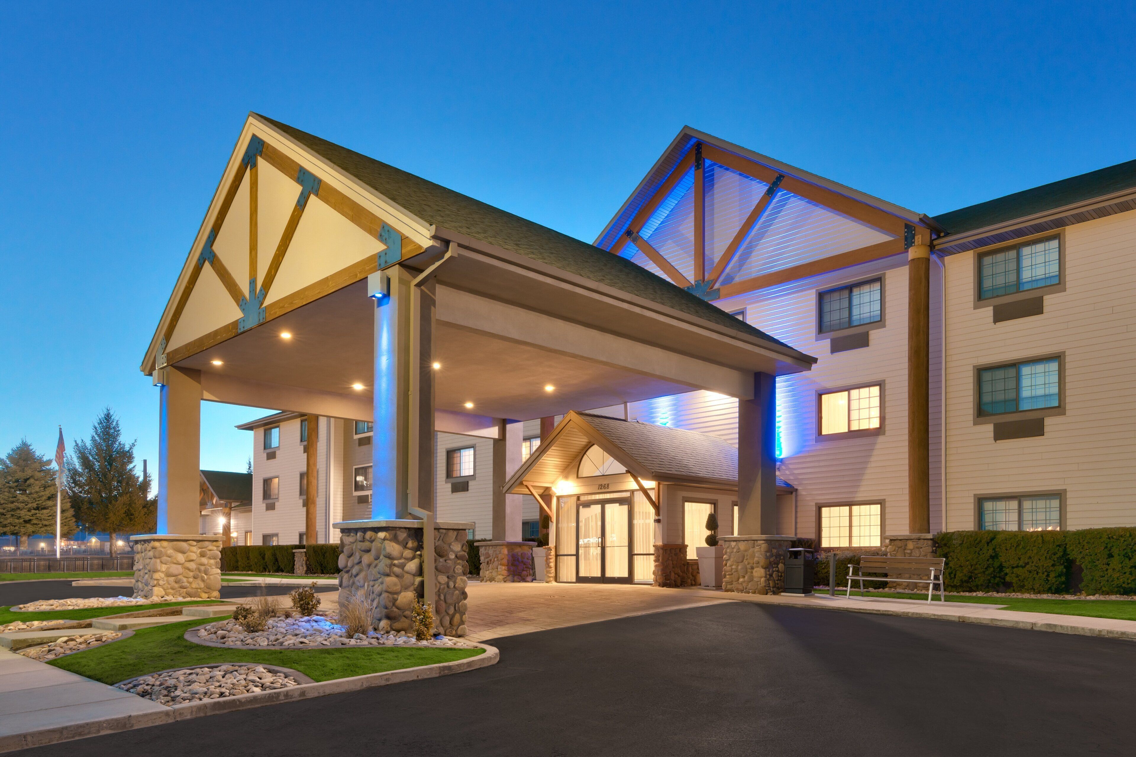A hotel entrance with a covered walkway, stone pillars, and a well-maintained lawn.