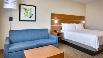 Une chambre d’hôtel avec un lit, un canapé bleu, une table de chevet en bois, une lampe et une œuvre d’art abstraite encadrée.