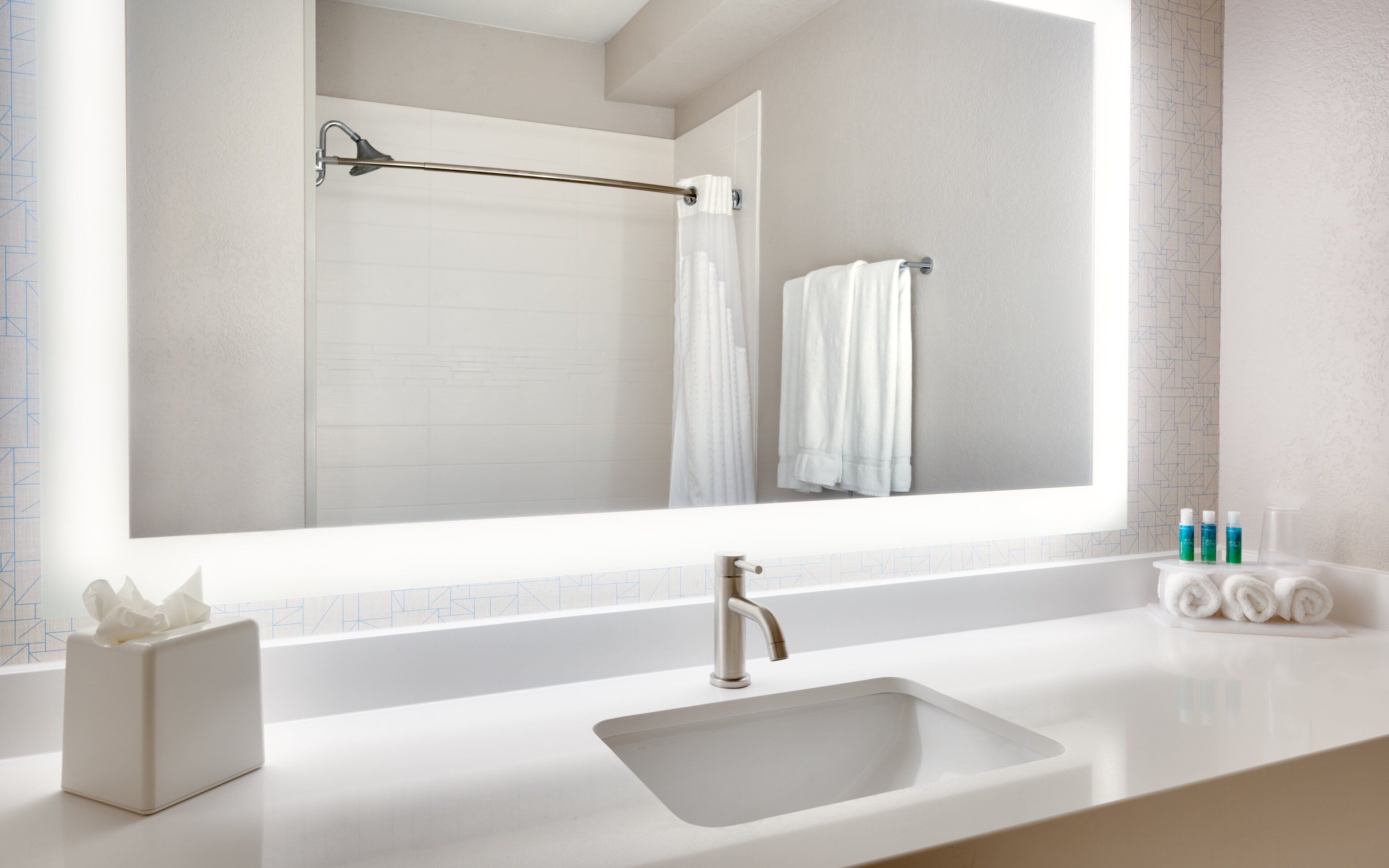 A bathroom with a large mirror, a sink, a towel rack, and a tissue box.