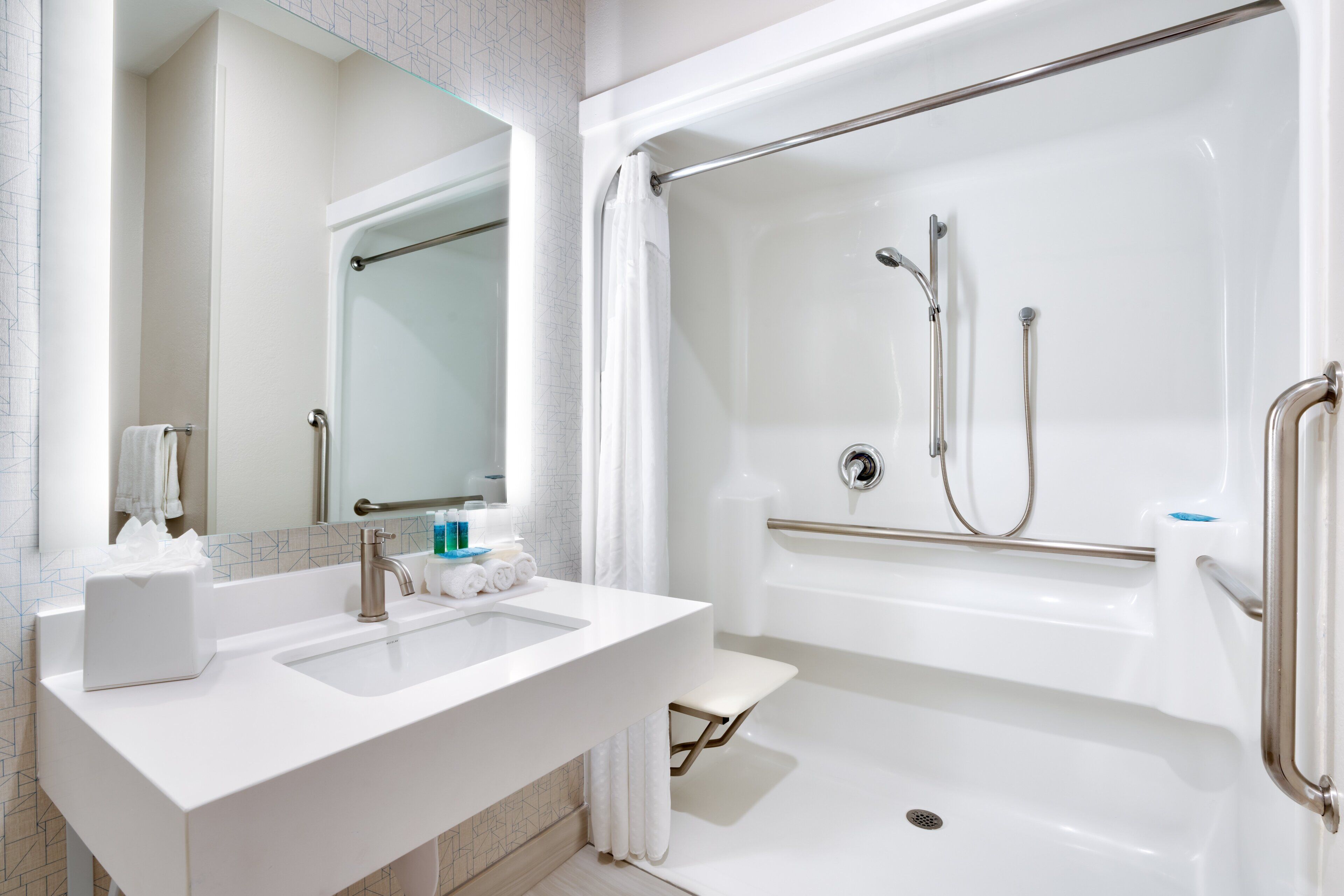 A modern bathroom with a white sink, a mirror, and a walk-in shower with grab bars.